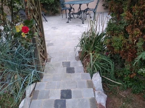 Escalier extérieur et pavage — Marches maçonnées, rampe métallique, pavés en pente douce.
