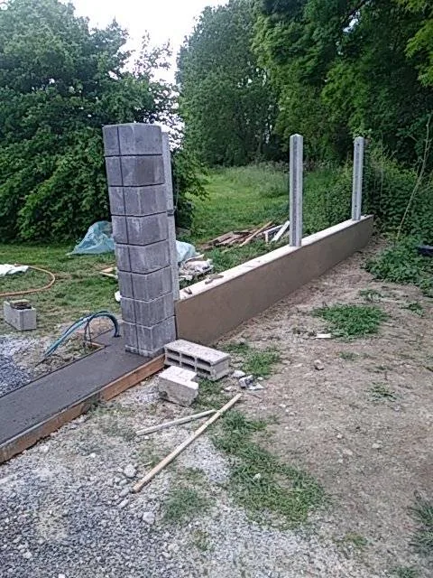 Muret de clôture en cours — Montage des blocs, ferraillage des piliers, avant enduit.