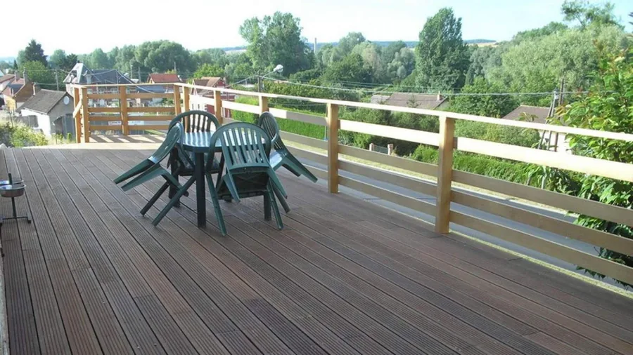 Terrasse bois sur pilotis — Un plancher en lames de bois posé au-dessus de la pente, garde-corps assorti, vue sur la vallée.