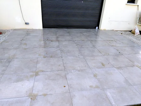 Terrasse carrelée · après — Une plateforme en gravier transformée en terrasse carrelée grand format, de plain-pied avec le garage.