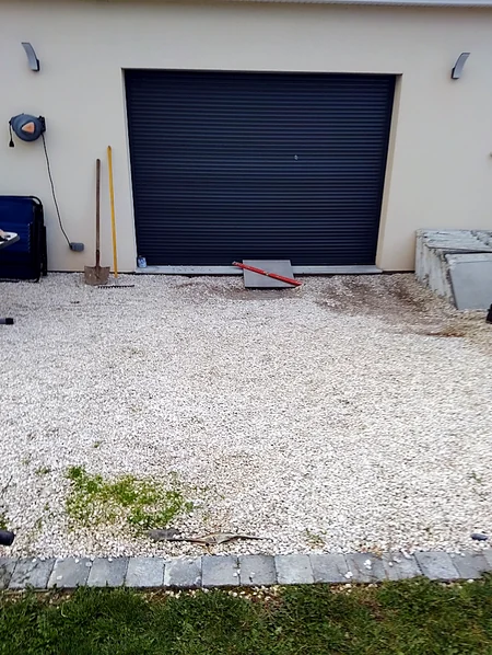 Le même endroit · avant — Avant travaux : gravier et herbe devant le garage. La dalle et la chape sont coulées avant la pose du carrelage.