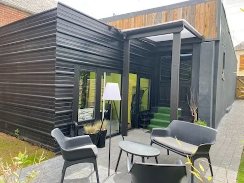 Terrasse de l'extension — Bardage sombre, salon extérieur.